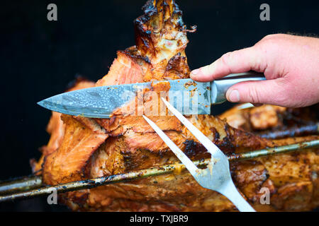 Chef Hände Schneiden ganze gegrillte Schweinefleisch für Steaks mit Messer. Vom Schwein gegrillte traditionelle Kohle und Feuer. Das kleine Schwein wird ganz auf einem offenen Feuer geröstet. P Stockfoto