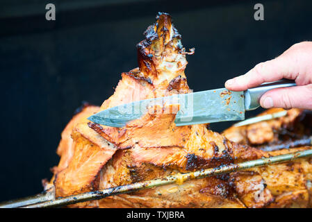 Chef Hände Schneiden ganze gegrillte Schweinefleisch für Steaks mit Messer. Vom Schwein gegrillte traditionelle Kohle und Feuer. Das kleine Schwein wird ganz auf einem offenen Feuer geröstet. P Stockfoto