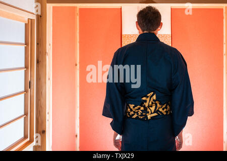 Traditionelle japanische Haus mit Schiebetür Fenster und Alkoven mit hängenden Blättern und roten Farbe mit Mann im Kimono beten Stockfoto