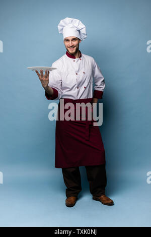 Gerne männliche Küchenchef stehend mit Platte auf hellblauem Hintergrund isoliert. Stockfoto