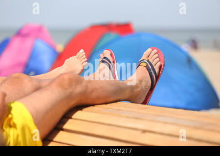 25. Juni 2019, Mecklenburg-Vorpommern, Warnemünde: Ein paar liegt auf einer Bank am Strand. Hohe Temperaturen im Sommer heute ziehen viele Touristen und Einheimische an die Ostsee. Foto: Danny Gohlke/dpa Stockfoto