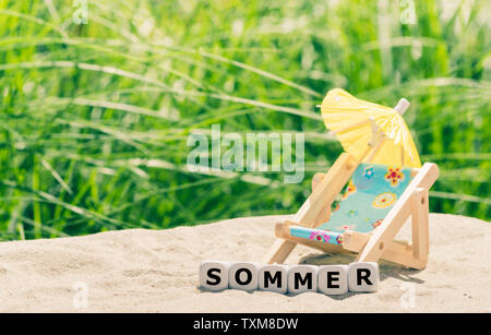 Sommer Konzept. Würfel auf einem Strand der deutschen Wort ommer' ('Summer' in Englisch) Neben einem Strandkorb. Stockfoto