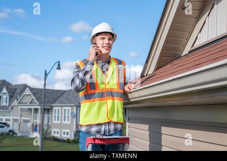 Der junge Architekt stand auf einer Leiter und über sein Handy. Stockfoto