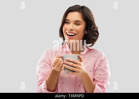 Glückliche junge Frau im Pyjama mit Becher Kaffee Stockfoto