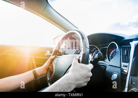 Autofahren, Schuß aus dem Beifahrersitz. Die männlichen Händen am Lenkrad eines modernen Fahrzeugs auf der Straße, gegen die Sonne Stockfoto