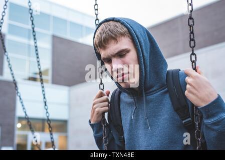 Traurige Teenager auf einer Schaukel sitzend außerhalb einer Schule. Er ist Erinnerungen über, als er jünger war. Stockfoto