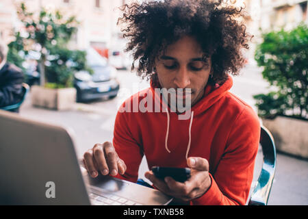 Junger Mann mit Smartphone und Laptop im Cafe Stockfoto