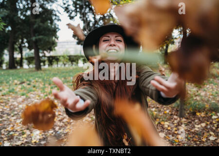 Junge Frau mit langen roten Haaren werfen Blätter im Herbst im Park Stockfoto