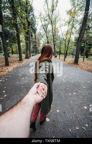 Junge Frau mit langen roten Haaren holding Freund Hand im Herbst Park, persönliche Perspektive Stockfoto