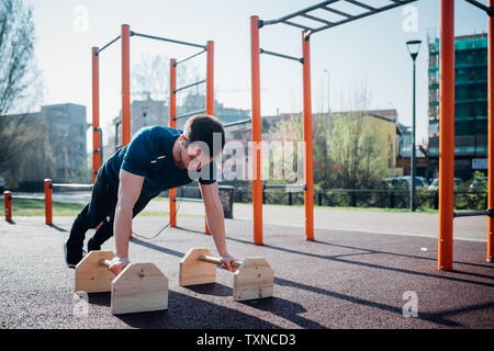 Calisthenics im Fitnessbereich im Freien, jungen Mann zu tun Push-ups auf Übung Ausrüstung Stockfoto