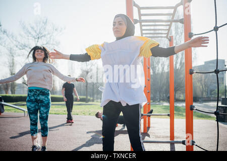 Calisthenics Klasse im Fitnessbereich im Freien, jungen Frauen springen mit ausgestreckten Armen Stockfoto