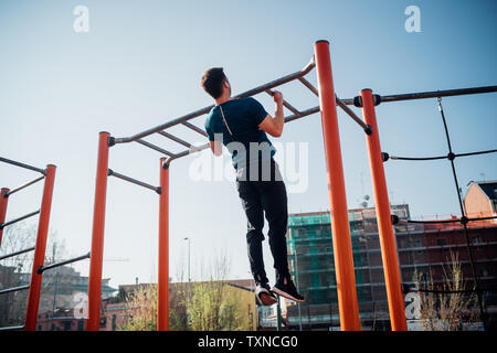 Calisthenics im Fitnessbereich im Freien, jungen Mann Zug tut ups auf Trainingsgeräten, Rückansicht Stockfoto