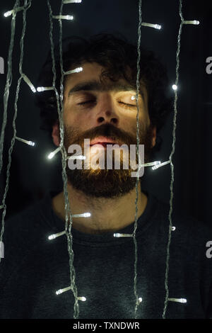 Junger Mann, der BÄRTIGE zwischen String für dekorative Leuchten Stockfoto