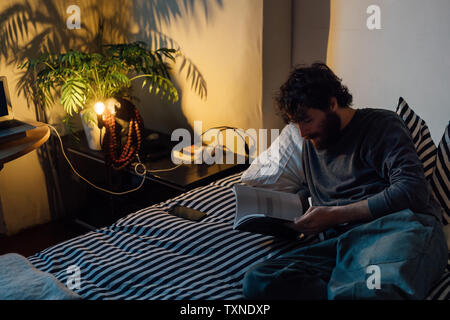 Junger bärtiger Mann lesen Buch im Bett Stockfoto