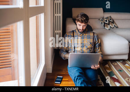 Mitte der erwachsene Mann sitzen auf Wohnzimmer Fußboden an Laptop suchen Stockfoto