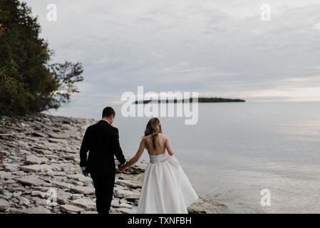 Romantische junge Braut und Bräutigam am Hochzeitstag am See entlang schlendern Stockfoto