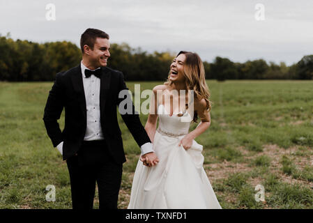 Romantische junge Braut und Bräutigam Hände halten und Lachen im Feld Stockfoto