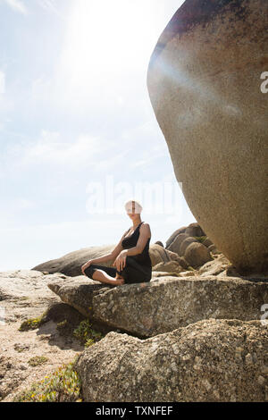Junge Frau üben Lotus yoga Pose am Strand Felsen, Porträt, Cape Town, Western Cape, Südafrika Stockfoto