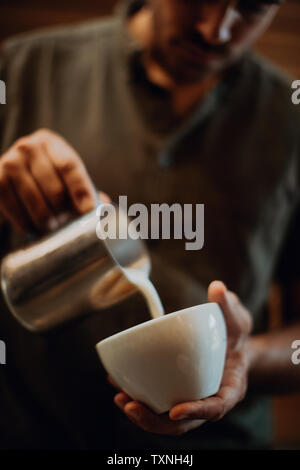 Barista gießen Milch in die Tasse Kaffee im Cafe, 7/8-flachen Fokus Stockfoto