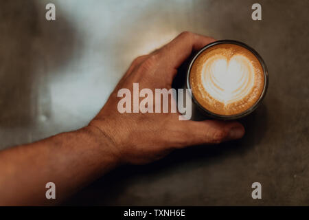 Barista Inverkehrbringen Tasse Latte mit Herz Form auf Cafe Zähler, Overhead Nahaufnahme von Hand Stockfoto