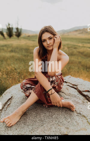 Schöne junge Frau sitzt im Schneidersitz auf Boulder, Porträt, Exeter, Kalifornien, USA Stockfoto