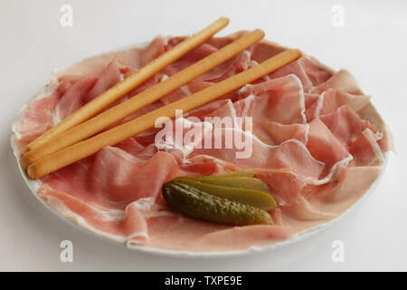 Teller köstliche frische Prosciutto di Parma (Parma Schinken) mit Brot klebt und in Scheiben geschnittene Gurken auf weißem Hintergrund. Stockfoto