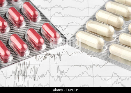 Nahaufnahme von Blister mit roten und weißen Pillen auf EKG-Diagramm. Stockfoto