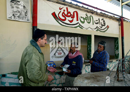 Eine palästinensische Soldat inspiziert palästinensische Arbeiter Dokumente. wie Sie darauf warten, durch die sehr zu Pass-befestigte israelische Sicherheit Station am 7. Dezember 2004, am Erez Checkpoint auf Israel aus dem Gazastreifen. Der Grenzübergang Erez hat strenge Sicherheitsmaßnahmen, die von den israelischen Behörden auferlegten. Rund 4.000 Palästinenser in israelischen und palästinensischen Fabriken in der industriellen Zone beschäftigt, während weitere 15.000 in der Regel berechtigt sind, in Israel zu arbeiten, obwohl die Grenze häufig vollständig aus Sicherheitsgründen gesperrt ist. (UPI Foto/Ismael Mohamad) Stockfoto