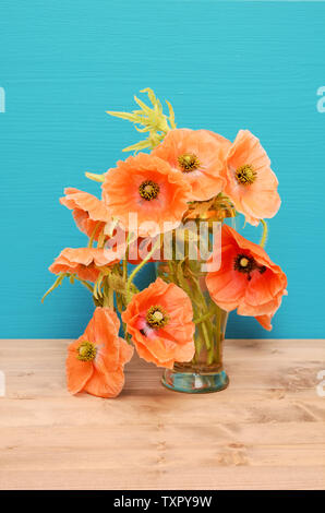 Vase mit beiläufig arrangiert blass rosa Mohnblumen auf einem hölzernen Tisch gegen einen türkisen Hintergrund Stockfoto
