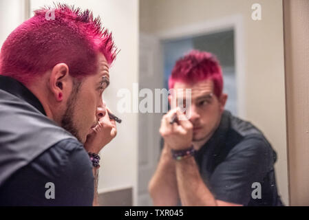 Diverse europäische männlich Mann mit pfennigabsatz rosa Haare Anwendung eyeliner Make-up im Spiegel Reflexion. Das Tragen von schwarzer Kleidung mit Punk Rocker alternative l Stockfoto