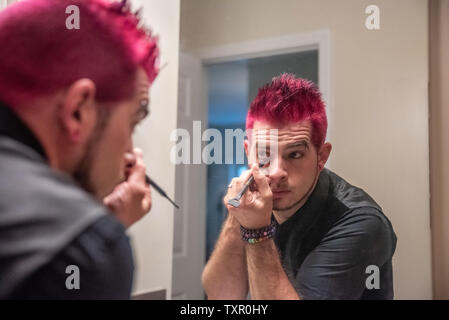 Diverse europäische männlich Mann mit pfennigabsatz rosa Haare Anwendung eyeliner Make-up im Spiegel Reflexion. Das Tragen von schwarzer Kleidung mit Punk Rocker alternative l Stockfoto