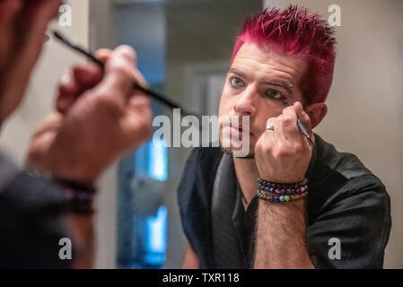 Diverse europäische männlich Mann mit pfennigabsatz rosa Haare Anwendung eyeliner Make-up im Spiegel Reflexion. Das Tragen von schwarzer Kleidung mit Punk Rocker alternative l Stockfoto