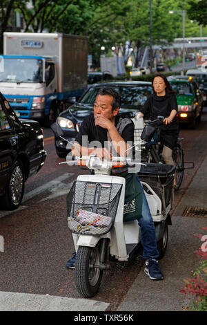 Tokio, Japan, 10. Mai 2019: Der Mann, der in den Verkehr auf einem Fahrrad warten, rauchen eine Zigarette. Stockfoto