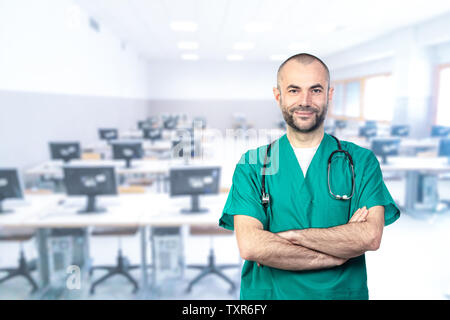 Porträts mit einem lächelnden Arzt tragen grüne Uniform, die Arme verschränkt und Computerraum im Hintergrund. Stockfoto