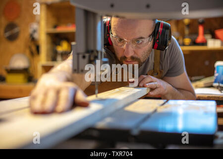 Detail eines Zimmermanns Absicht auf einem Stück Holz mit Präzision mit einer Bandsäge. Stockfoto