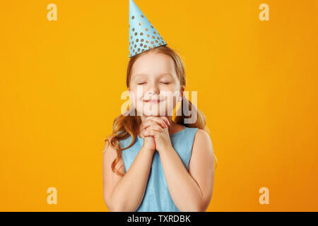 Süße kleine Mädchen feiert Geburtstag. Das Kind schloss die Augen und machte einen Wunsch. Closeup Portrait auf gelben Hintergrund. Stockfoto