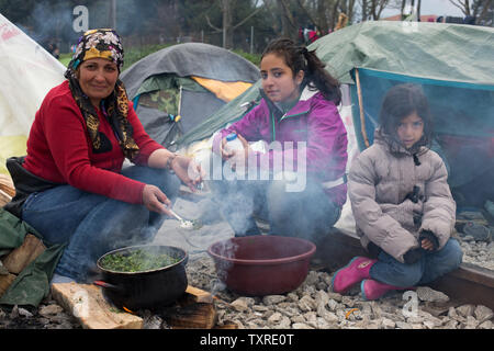 Eine Familie aus dem Irak, eine ältere Frau und zwei jungen Mädchen, sind Kochen außerhalb ihrer Hütte in einem Flüchtlingslager in Griechenland. Mütter, Kinder und Familien gehören zu den 12.000 Flüchtlinge in einem provisorischen Lager in Idomeni, Griechenland gestrandet, an der Grenze zu Mazedonien im April 2016 nach der Grenze geschlossen wurde. Foto von David Caprara/UPI Stockfoto