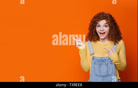 Curly rothaarige Frau, die überrascht, Gesicht und Hände in Leere orange hinterlegt. Wow es ist erstaunlich Stockfoto