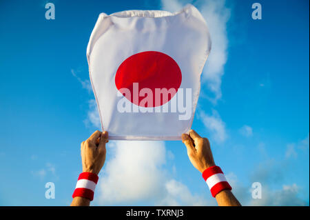 Hände mit Japan Rot und Weiß Armband mit einem japanischen Fahne winken in hellen, sonnigen blauen Himmel Stockfoto