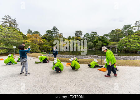 Kyoto, Japan - 17. April 2019: Freiwillige im Garten arbeitende Arbeiter trennt die weißen und schwarzen Kies von grünen Frühling Garten im kaiserlichen Palast mit Lak Stockfoto