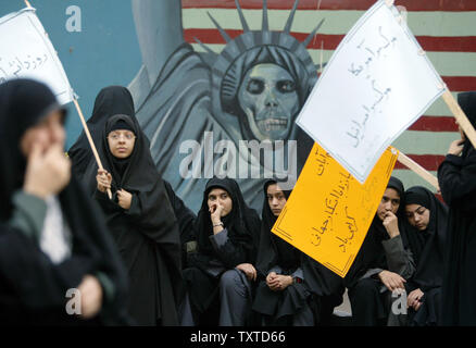 Iranische Frauen halten Plakate vor einer anti-amerikanischen Wandbild "Schüler Tag' vor der alten US-Botschaft in Teheran am 4. November 2006 zu gedenken. Militante Studenten stürmten in der Botschaft am 4. November 1979 und 52 Amerikanern Geisel für 444 Tage. (UPI Foto/Mohammad Kheirkhah) Stockfoto