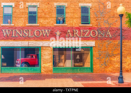 Winslow Arizona, USA 5/16/2016. Seite von Gebäude mit Kunst arbeiten, Windows, Menschen umarmen, Adler, LKW-Pritsche Ford mit weiblichen Treiber. Stockfoto