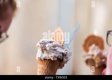 Frau hand Weiße Vanille Karamell Eis gelato Kegel mit Bokeh verschwommenen Hintergrund und Löffel Stockfoto