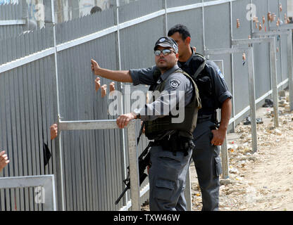 Israelische Grenzpolizisten stand durch einen Zaun ausblenden Palästinenser wartet das israelische Militär checkpoint aus Bethlehem, 5. Oktober 2007, nach Jerusalem zu überqueren. Ein israelischer Schließung auf der West Bank dürfen nur Männer über 50 Jahre und Frauen über 40 Jahre alt Geben Sie Jerusalem an der Al Aqsa Moschee, die drittheiligste Ort des Islam zu beten, für Ramadan Freitag Gebeten. (UPI Foto/Debbie Hill) Stockfoto