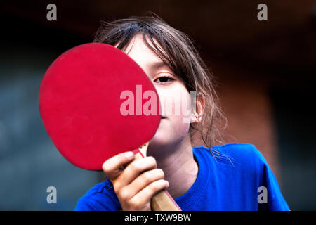 Junge versteckt sein Gesicht hinter Tischtennis bat. Stockfoto