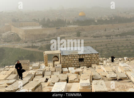 Ultra-orthodoxe Juden weg, während ein Sandsturm auf dem Friedhof auf dem Ölberg in Jerusalem, mit Blick auf den Felsendom in der Altstadt von Jerusalem, 11. Februar 2015. Die israelische Umweltschutz Ministerium berichtet, dass der Sandsturm durch das Land fegt verursacht hat die Luftverschmutzung die höchsten in den letzten fünf Jahren zu werden. Foto von Debbie Hill/UPI Stockfoto