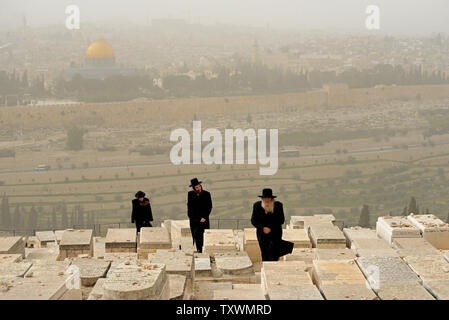 Ultra-orthodoxe Juden weg, während ein Sandsturm auf dem Friedhof auf dem Ölberg in Jerusalem, mit Blick auf den Felsendom in der Altstadt von Jerusalem, 11. Februar 2015. Die israelische Umweltschutz Ministerium berichtet, dass der Sandsturm durch das Land fegt verursacht hat die Luftverschmutzung die höchsten in den letzten fünf Jahren zu werden. Foto von Debbie Hill/UPI Stockfoto