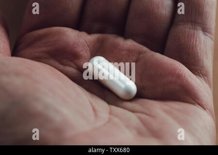 Nahaufnahme einer Hand, die eine weiße Kapsel Pille Stockfoto