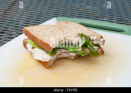 Teilweise gegessen Truthahnsandwich auf Brot aus Weizen liegen auf einem Schneidebrett mit Salat und Brot aus Weizen. Stockfoto