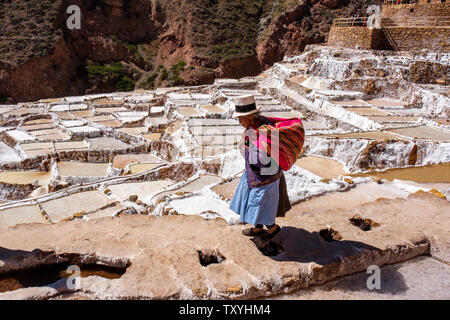 Lokale peruanische Frau gehen auf Salineras de Maras/Maras Salzminen. Die Salzgewinnung in Maras Salinen, Terrassen und Teichen, Peru Sacred Valley. Stockfoto